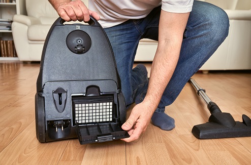 Homme ouvrant un aspirateur pour accéder à son filtre